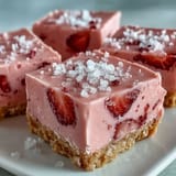 A square of No-Bake Strawberry Fudge Squares is lifted on a spatula, revealing the crunchy graham cracker crust base.