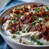 Steaming bowl of homemade Loaded Potato Soup featuring velvety russet potatoes, cheese, bacon crumbles, and garnishes.