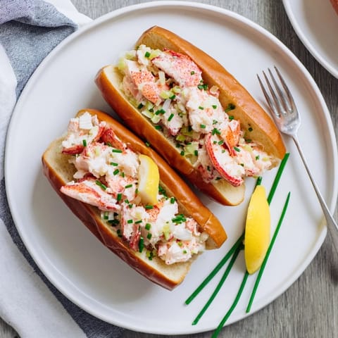 A close-up of a toasted split-top bun overflowing with succulent lobster, served beside a bright lemon wedge.