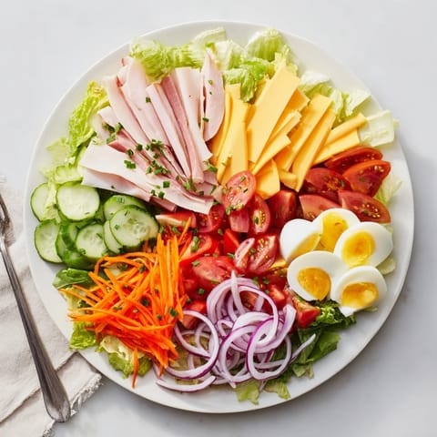 Hearty Chef Salad arranged on a platter with neatly stacked strips of ham and turkey, cubed Swiss and cheddar cheeses, quartered hard-boiled eggs, fresh carrot ribbons, and crisp red onion slices.