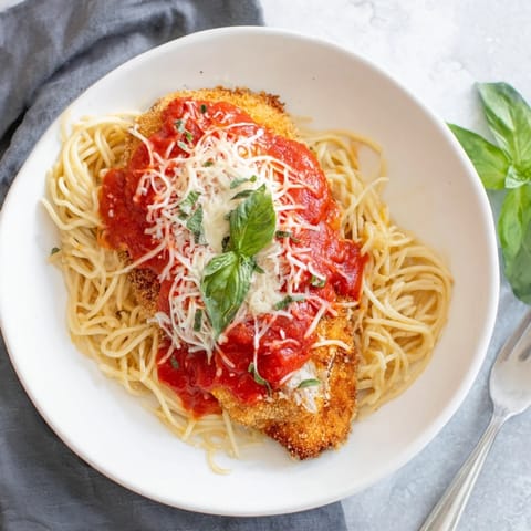 Homemade Chicken Parmesan baked until bubbling and golden, ready to be plated over a bed of marinara pasta.