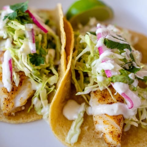 Flaky white fish fillets nestled in soft tacos with shredded cabbage, vibrant red onion, and a dollop of creamy sauce, ready to serve.
