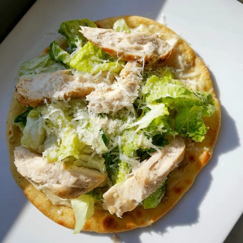 Sliced Chicken Caesar Flatbread on a wooden board, topped with parmesan and cherry tomatoes for a light lunch.  