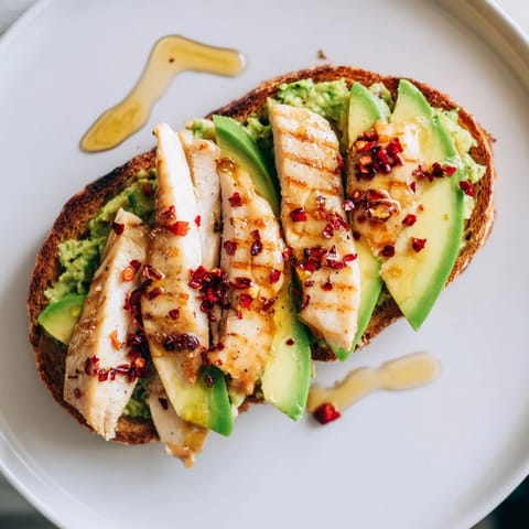 Smashed avocado chicken toast garnished with fresh herbs and chili flakes, served warm with a drizzle of honey.  