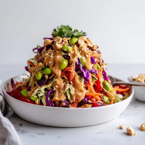 Overhead view of a colorful Thai Peanut Salad with shredded purple and green cabbage, carrots, and edamame, topped with chopped peanuts and sesame seeds.