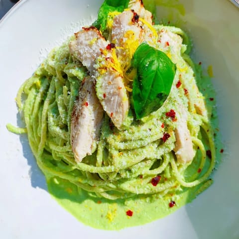 Creamy Avocado Chicken Pasta served on a white plate, featuring sliced grilled chicken atop silky green sauce-coated spaghetti, garnished with fresh basil and lemon zest.