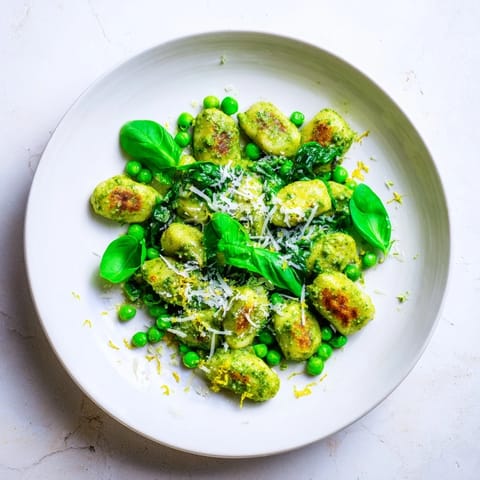 A close-up of fragrant Pesto Pea Gnocchi Skillet, with fresh basil leaves and lemon zest garnishing the colorful, steaming meal.