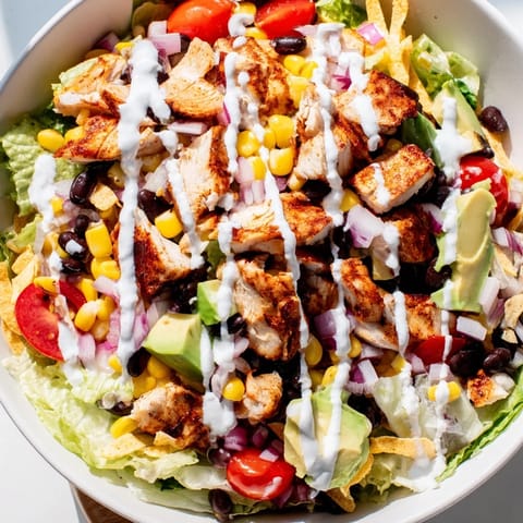 Freshly tossed Chicken Taco Chopped Salad with juicy taco-seasoned chicken, crunchy tortilla chips, cherry tomatoes, red onion, and shredded cheddar, ready to serve on a wooden table.  
