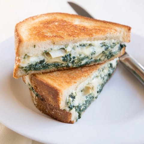 A creamy Artichoke Spinach Grilled Cheese on crisp sourdough, perfect with a bowl of tomato soup.