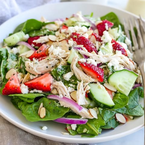 Vibrant Strawberry Poppy Seed Chicken Salad with juicy berries, crunchy almonds, and feta crumbles on a bed of mixed greens.  