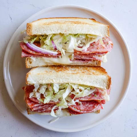 A close-up of an Italian Sub Grilled Cheese shows melted provolone oozing from crusty, buttery bread with colorful cold cuts.