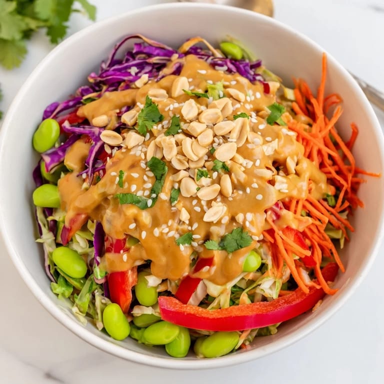 A refreshing vegan Thai Peanut Salad served in a white bowl, garnished with fresh cilantro, scallions, and extra lime wedges for bright flavor.
