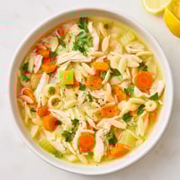 Tender shredded chicken and orzo pasta swim in a bright, steaming lemon pepper broth in a rustic bowl.  