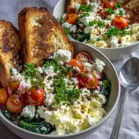 A close-up view of a vibrant Spinach and Feta Breakfast Bowl, featuring fluffy scrambled eggs, wilted spinach, and juicy halved cherry tomatoes.